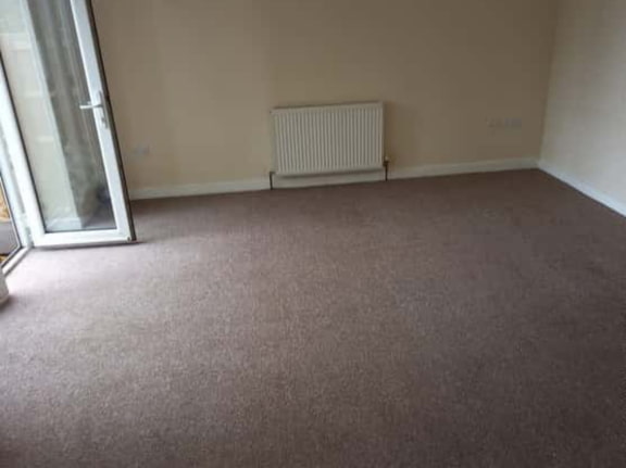 This is a photo of a living room after it has been cleaned. The room is empty and has a brown carpet that has been steam cleaned works carried out by Buckhurst Hill Carpet Cleaning